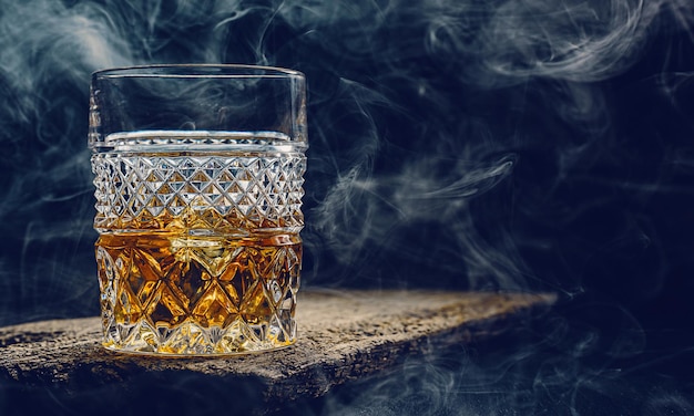 Verre de whisky avec de la glace sur une table en bois entourée de fumée