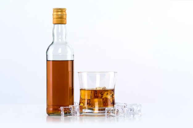 Verre de whisky avec des glaçons et une bouteille sur un mur blanc