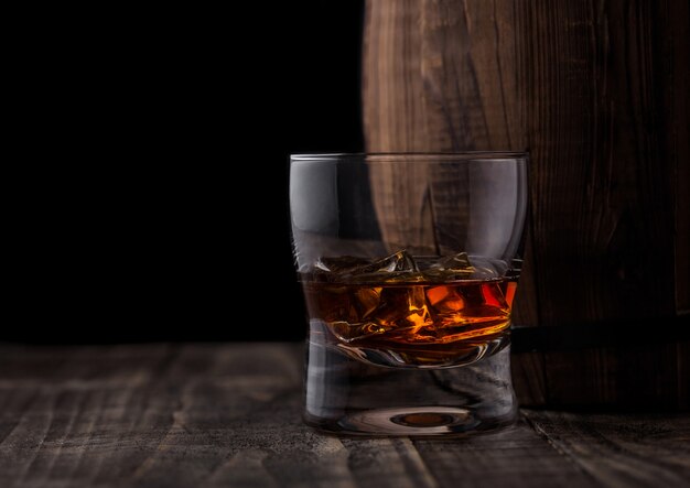 Verre de whisky avec des glaçons à côté du tonneau en bois