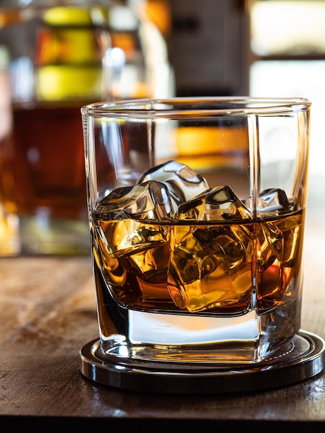 Verre de whisky sur les rochers sur un bar en bois avec des bouteilles en arrière-plan