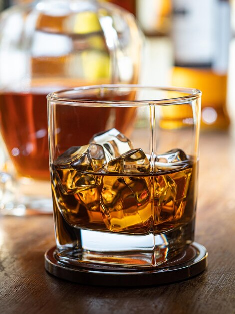 Photo verre de whisky sur les rochers sur un bar en bois avec des bouteilles en arrière-plan