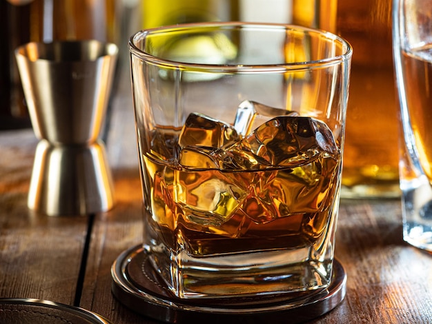 Verre de whisky sur les rochers sur un bar en bois avec des bouteilles en arrière-plan