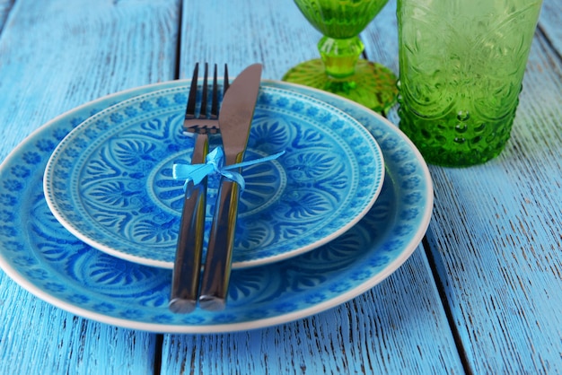 Verres à assiettes colorées vides et argenterie sur table en bois