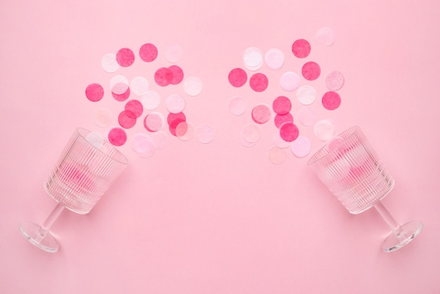 Verres à champagne avec des confettis roses sur fond de papier de couleur rose style minimal. Composition à plat pour anniversaire, fête des mères ou vue de dessus de mariage