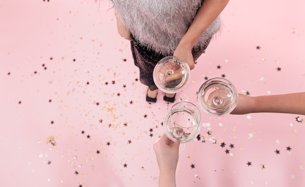 Verres à champagne dans les mains des filles lors d'une fête sur fond rose, espace de copie.