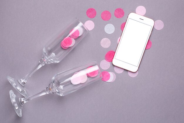 Verres de Champagne et téléphone portable avec des confettis roses sur gris