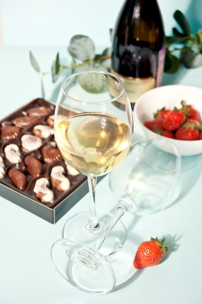 Verres de champagne ou de vin de raisin blanc avec assiette de chocolats et fraises, bouteille sur le fond.