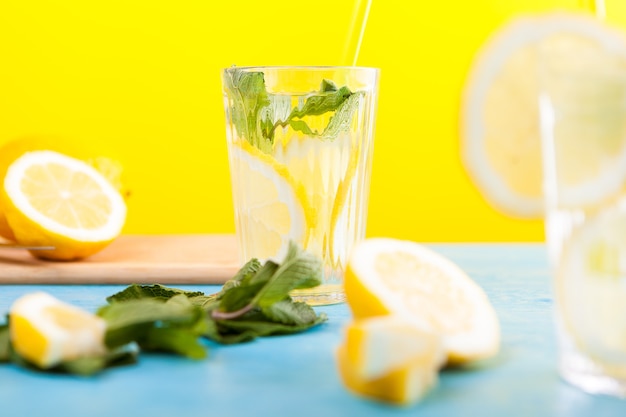 Verres avec de l'eau de désintoxication fraîche faite maison avec des citrons sur fond jaune assis sur une table bleue