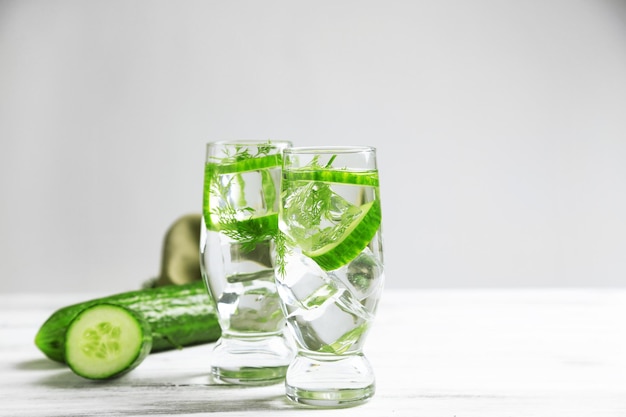 Verres avec de l'eau fraîche de concombre biologique sur une table en bois sur fond gris