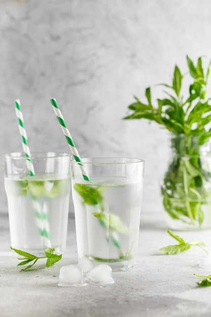 Verres d'eau froide avec des feuilles de menthe fraîche et des glaçons sur du béton gris