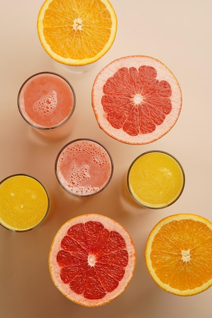 Verres de jus d'agrumes avec des fruits tranchés sur fond pastel