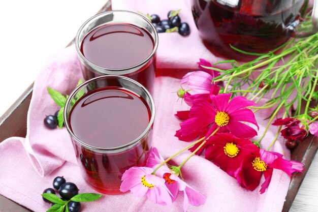 Verres de jus de cassis frais sur plateau en bois avec serviette rose et gros plan de fleurs