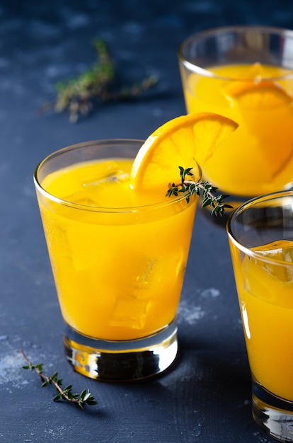 Verres de jus d'orange avec des feuilles de thym et une tranche d'orange sur fond bleu