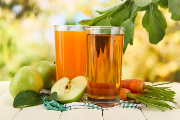 Verres de jus de pommes et de carottes sur une table en bois blanche sur fond vert