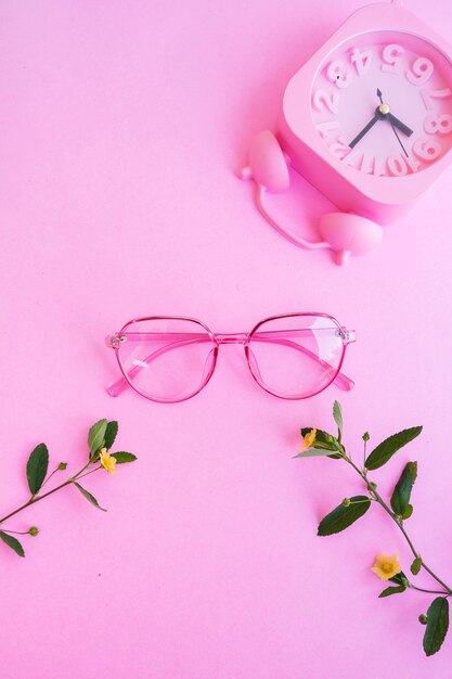 Verres ovales sur la photo dans un style estival minimal sur fond de couleur rose pastel. réveil, fleurs jaunes et feuilles vertes