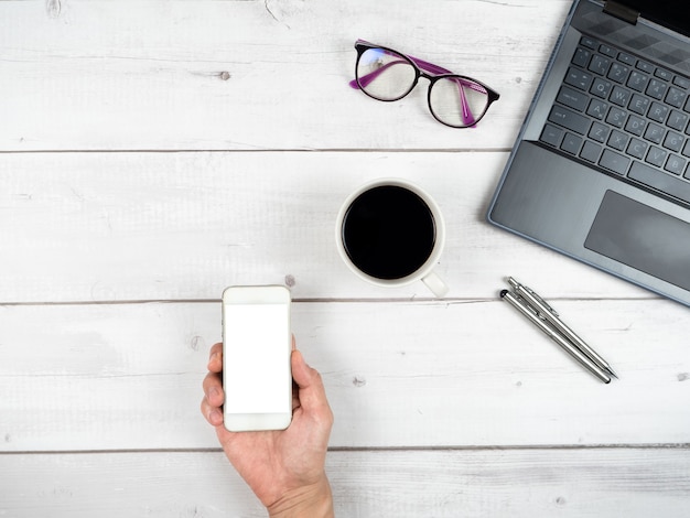Verres pour ordinateur portable tasse à café et deux stylos en argent vue de dessus de l'espace de travail et prise de main smartphone Pentecôte