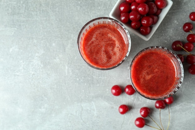 Verres de smoothie aux cerises et ingrédients sur une table texturée grise