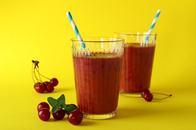 Verres de smoothie cerise et ingrédients sur fond jaune