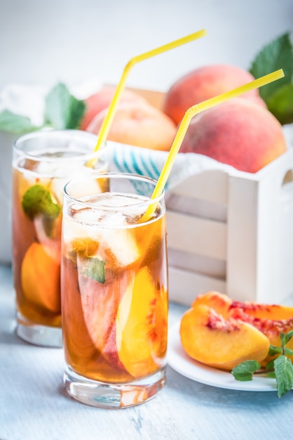 Verres avec thé glacé fait maison, tranches de pêche aromatisées à la pêche et fraîchement coupées.