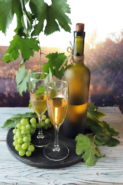 Verres de vin blanc, une grappe de raisin sur une table en bois, sur fond de coucher de soleil