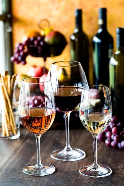 Des verres de vin rouge et blanc rose avec des bouteilles de vin et des fruits à l'arrière