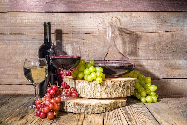 Verres de vin rouge et blanc avec soleil et ombres, avec bouteille et carafe, grappe de raisin, sur fond en bois avec socles bio, récolte d'automne, concept de cave