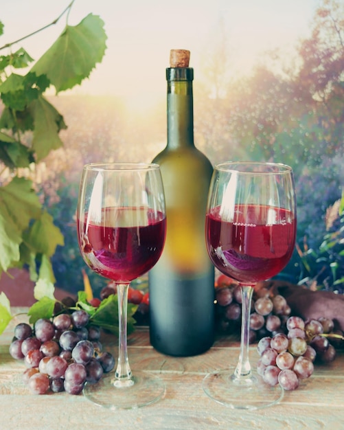 Verres de vin rouge jeune, une grappe de raisin sur une table en bois, sur fond de coucher de soleil