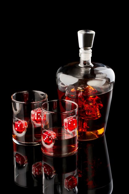 Verres à whisky avec rhum ou whisky avec dés rouges et carafe avec godille sur fond de verre foncé