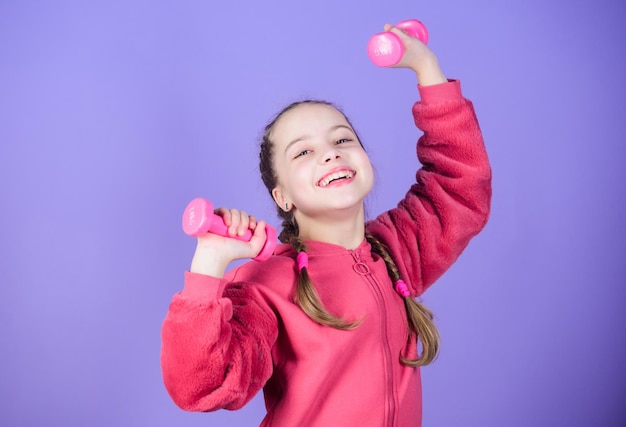 Vers un corps plus sain Concept de réadaptation Fille exerçant avec haltère Enfant tenir petit fond violet haltère Exercices d'haltère débutant Sport pour les adolescents Exercices faciles avec haltère