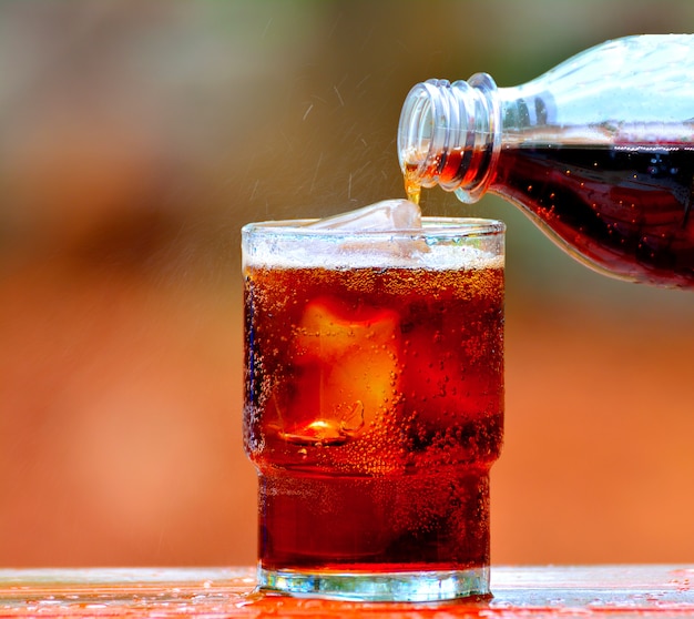 Verser le cola dans un verre de glace sur fond flou.