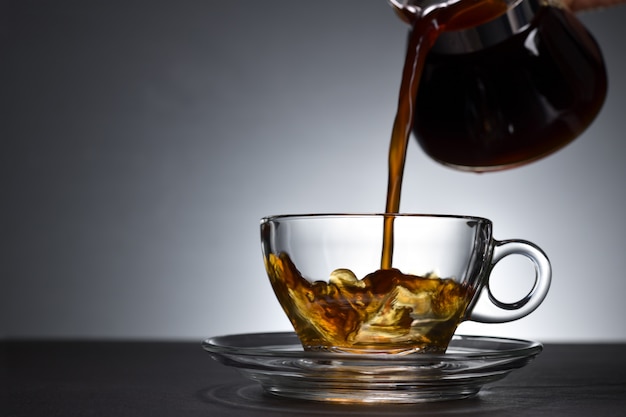 Verser du café sur une tasse transparente sur fond noir