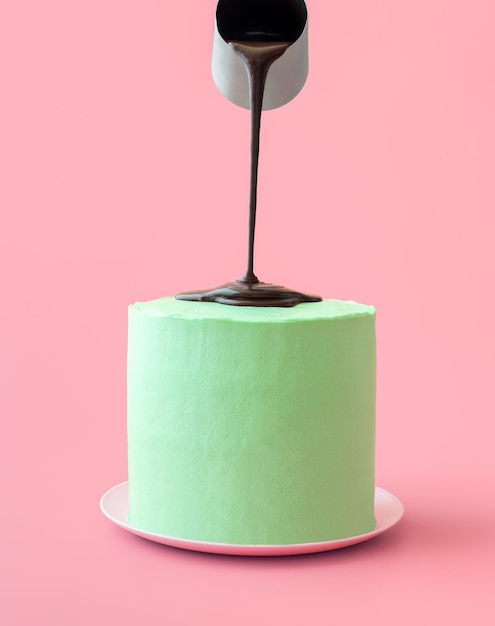 Photo verser du chocolat fondu sur un gâteau à la menthe poivrée isolé sur fond rose