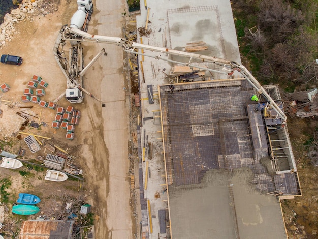 Verser du ciment de béton sur le toit d'un immeuble résidentiel en construction à l'aide d'un camion-pompe à béton à flèche haute pour fournir le mélange aux étages supérieurs Vue aérienne