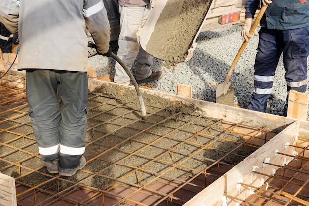 Verser du ciment ou du béton avec un chantier de construction de camion malaxeur à béton avec une fondation de grillage renforcée Les travailleurs installent et nivellent le béton dans la fondation