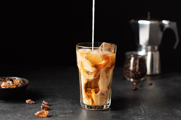 Verser du lait dans un verre avec du café glacé sur fond noir Boisson d'été rafraîchissante froide