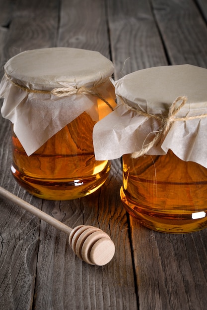 Verser du miel aromatique dans un bocal, gros plan. Miel en pots de verre et cire en nid d'abeilles sur table en bois.