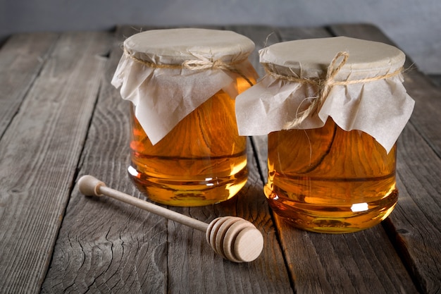 Verser du miel aromatique dans un bocal, gros plan. Miel en pots de verre et cire en nid d'abeilles sur table en bois.