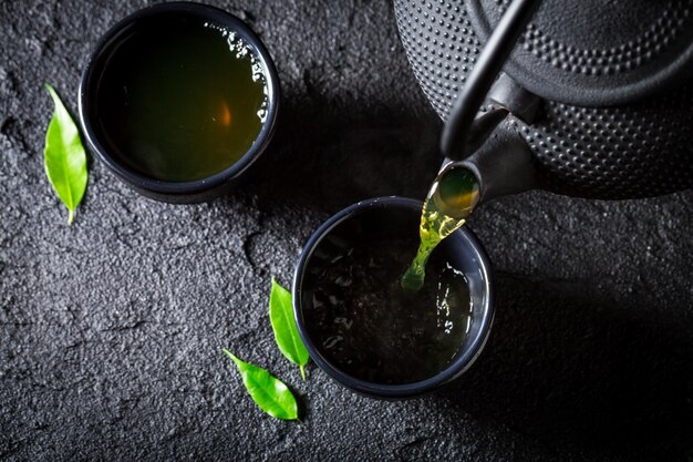 Verser du thé vert dans une tasse sur une roche noire