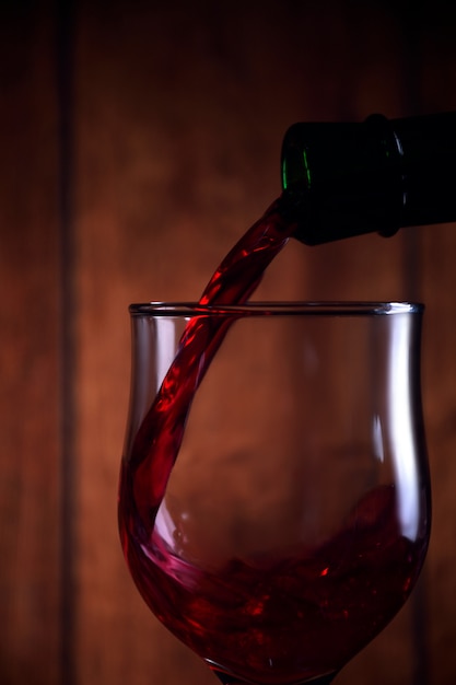 Verser du vin rouge dans le verre sur fond rustique en bois