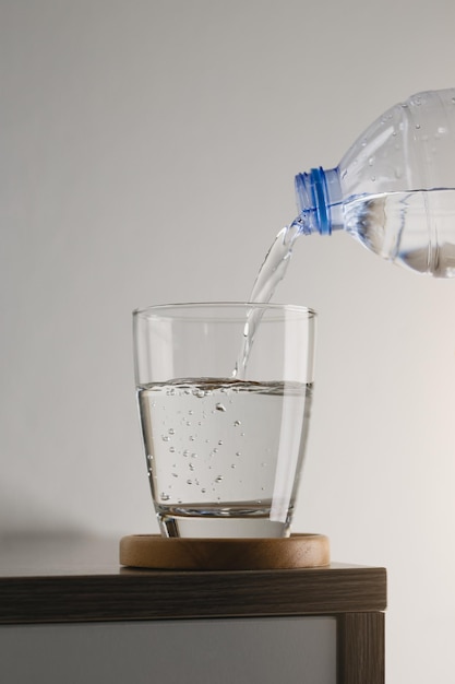 Verser de l'eau d'une bouteille en plastique en verre sur une table en bois
