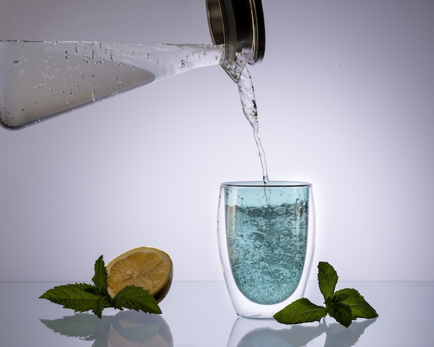 Verser de l'eau dans le verre de la carafe en verre sur fond bleu clair transparent, boire de l'eau propre, concept.