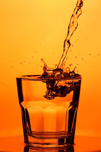 Verser de l'eau dans un verre. Éclaboussure d'eau dans un verre sur fond orange