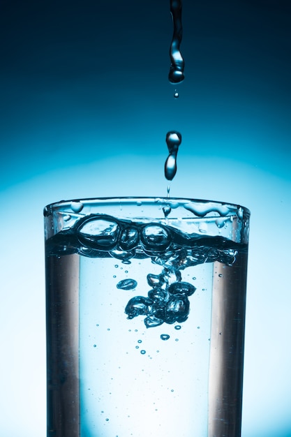 Photo verser de l'eau dans le verre sur fond bleu.