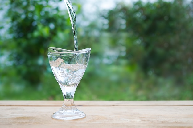 Verser de l'eau pure dans un verre sur bois avec image floue de laisser vert.