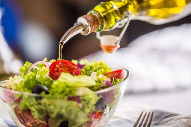 Verser de l'huile d'olive dans un bol de salade de légumes frais.