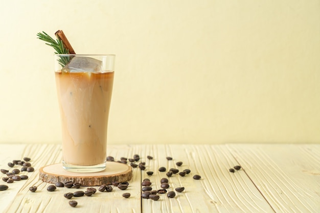 Verser le lait dans un verre à café noir avec glaçon, cannelle et romarin sur table en bois