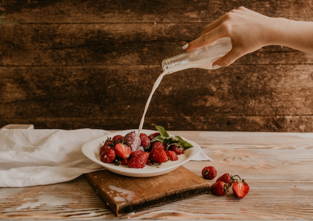 Verser le lait à la main sur les fraises rouges en plaque blanche