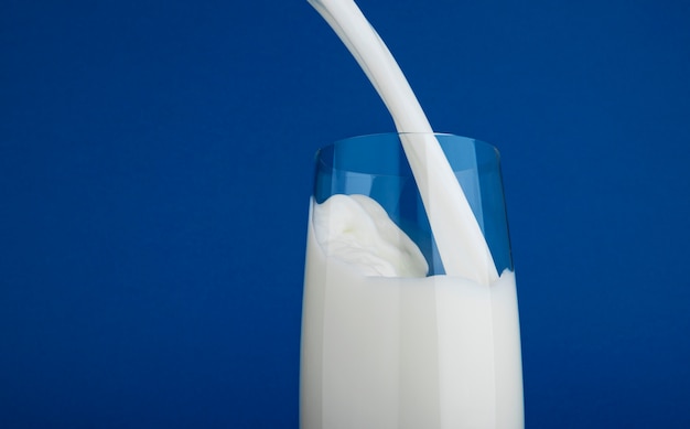 Verser le lait en verre isolé sur fond bleu