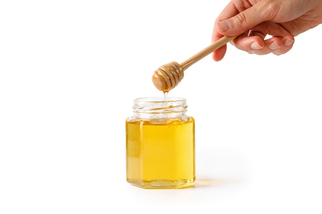 Verser le miel Main de femme tenant une cuillère à miel en bois avec du miel liquide isolé sur un blanc