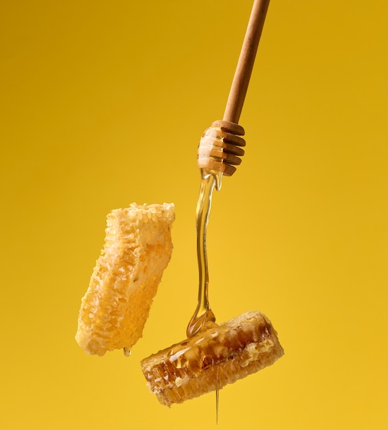 Verser le miel sucré transparent d'un bâton en bois sur un nid d'abeilles en cire. Fond jaune. La nourriture lévite